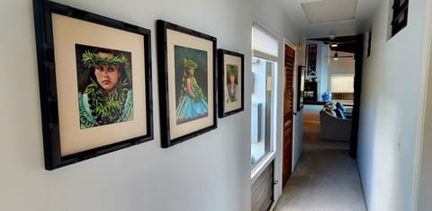 Hallway from primary and guest bedrooms on the main floor looking into living area and kitchen. Beautiful artwork may be enjoyed throughout the house.