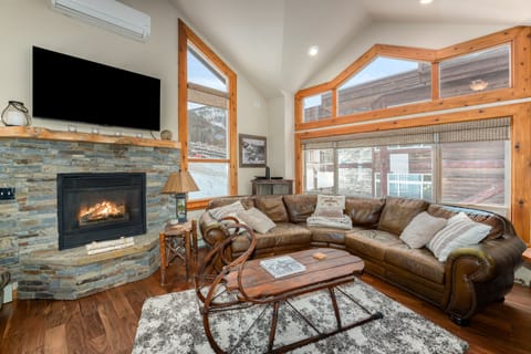 Living Area with Cozy Furnishings Including A Leather Sectional Sofa, Stone Fireplace, and a Smart TV