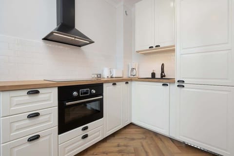 A modern kitchen with white cabinetry, a wooden countertop, and a sleek range hood.

