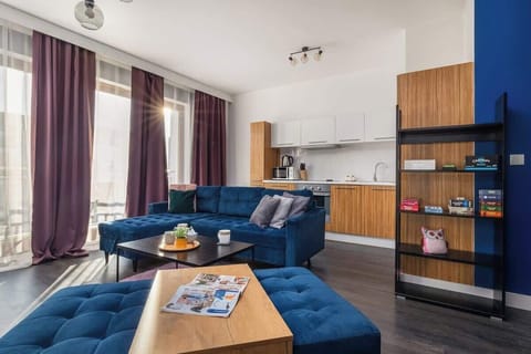 Spacious and bright living room.A spacious, stylishly furnished living room with a blue sofa bed and a standing coffee table in the centre of the room. Two navy blue poufs can be seen in the foreground. Curtains and drapes hang in the windows, giving