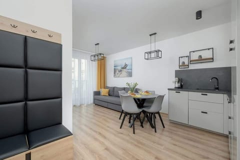 A view from the hallway into the apartment, highlighting a black upholstered wall panel and the open-concept kitchen and dining area.