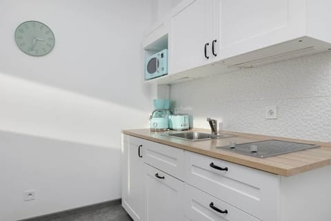 A compact yet fully equipped kitchen with sleek white cabinetry, a modern countertop, and pastel-colored kitchen appliances that enhance its stylish design.