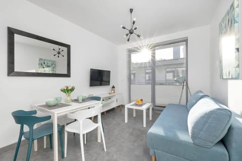 A bright and stylish space with a modern blue sofa, a dining table with chairs, and a TV.