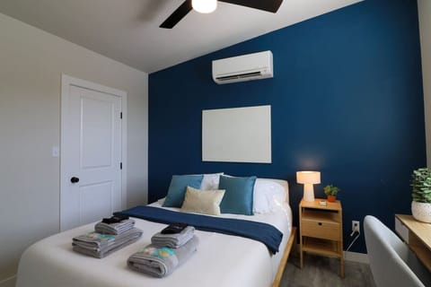 Master bedroom with a striking navy blue accent wall. Sink into the plush embrace of a linen-upholstered queen bed dressed in cozy cotton sheets. Ample storage in the closet with hangers, iron, ironing board, luggage rack, pillows, and board games.
