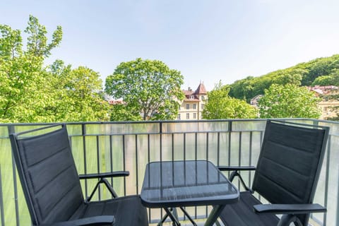 A top-down angle of the balcony setup with seating, offering a view of a neatly maintained garden area and surrounding residential buildings.