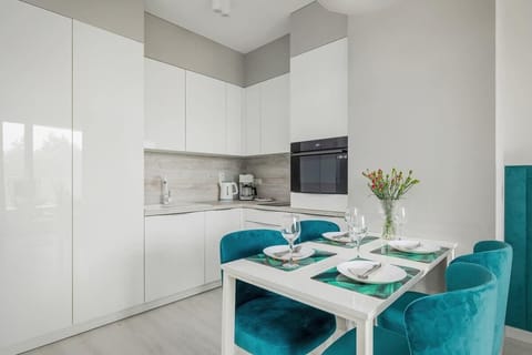 A well-organized kitchen with high-gloss white cabinets, a compact yet functional layout, and a small dining table.

