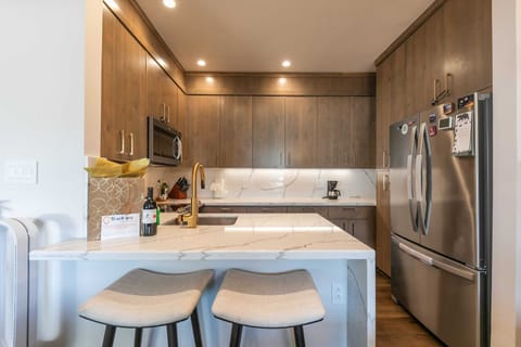 The modern kitchen has ample counter space, sleek marble countertops, and a kitchen bar with 2 bar stools.