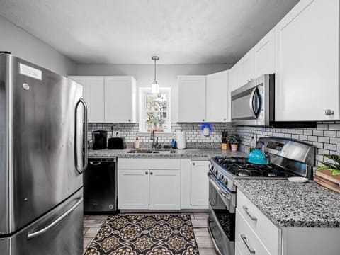 Bright, modern kitchen with crisp white cabinets, granite countertops, and subway tile backsplash. Stainless appliances and patterned wood-look floors flow seamlessly into the adjacent dining room for effortless entertaining! 🍽️✨🏡