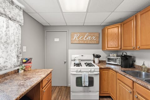 Well-appointed L-shaped kitchen with warm oak cabinets, granite-look countertops, a gas stove, and a double sink under ample cabinet storage. Cozy sign invites you to unwind as you cook and connect. 🍳🏡✨