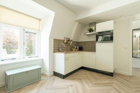 Adjacent is a modern kitchen with a compact design, featuring white cabinetry and a tiled backsplash, creating a welcoming and practical cooking space.