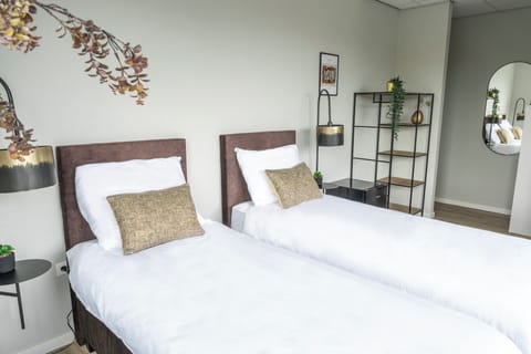 Minimalist bedroom featuring twin beds, elegant bedside lighting, soft curtains, natural greenery accents, and a spacious window overlooking urban scenery.