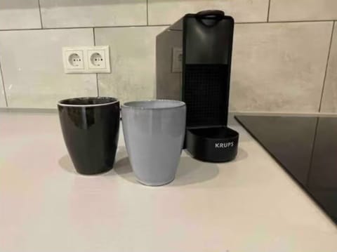 featuring a Krups coffee machine, two stylish mugs in black and gray, tiled backsplash, and sleek neutral tones for a clean, contemporary look.