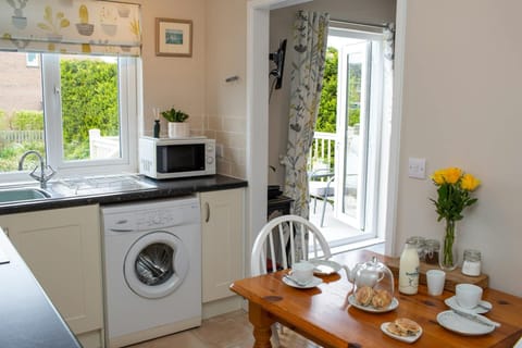 open kitchen with dining table, washing machine, microwave with plant on top and sink under window