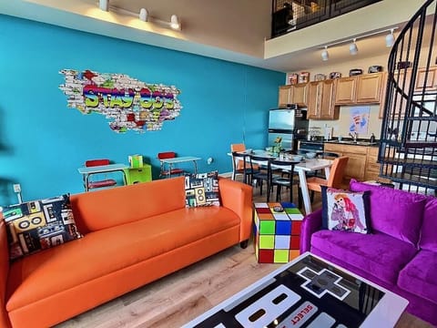 Unwind in our cozy living area featuring a Nintendo coffee table, Rubik’s cube end table, and a comfortable leather couch. Immerse yourself in 80s nostalgia with playful decor and vibrant colors for a truly unique experience.