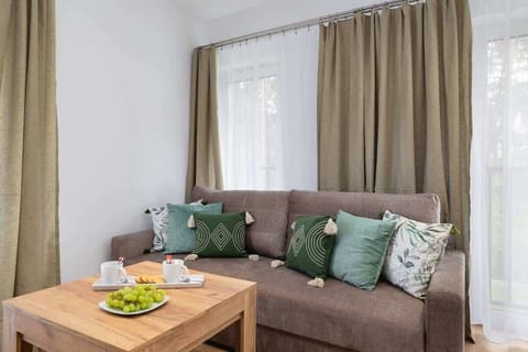 A bright living room with a brown sofa decorated with green-toned cushions. A fruit plate is placed on the coffee table, adding a cozy touch to the space.