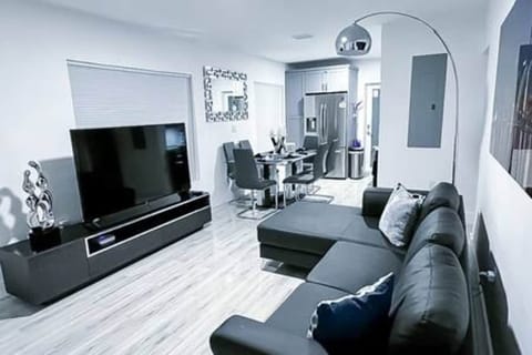 Modern, open-concept living space featuring a sleek sectional, large flat-screen TV, and contemporary decor. Adjacent dining area and fully equipped kitchen make it perfect for a relaxing and convenient stay. Ideal for comfort and style.