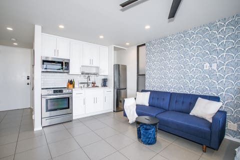 A stylish and compact studio apartment featuring a fully equipped modern kitchen, a cozy blue sofa, and chic decor with a striking blue accent wall, creating a perfect blend of comfort and functionality.