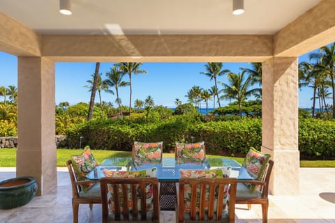 Covered lanai dining table surrounded by lush tropical gardens with a peek of the Pacific.