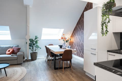 A spacious living and dining area with a comfortable sofa, plants, and a cozy dining table under the skylights.