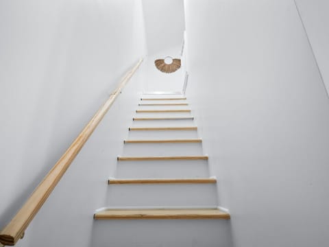 Bright staircase with light wood steps and simple design - Minimal Airbnb style with warm natural light above - Leading guests to private upper-level bedrooms
