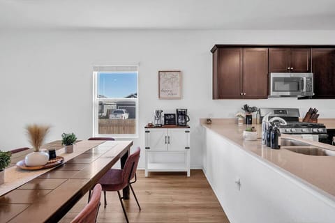 Bright and modern kitchen and dining area featuring a large wooden table with stylish seating for six. The kitchen is fully equipped with stainless steel appliances, a coffee station, and ample counter space—perfect for cooking and gathering.