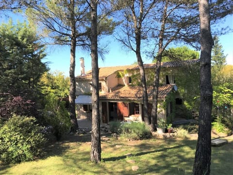 The villa is nestled amongst tall pine trees, offering privacy and a tranquil setting. The exterior of the house boasts a charming terracotta roof and a spacious garden with a glimpse of a patio. The home is surrounded by lush greenery, promising a peacef