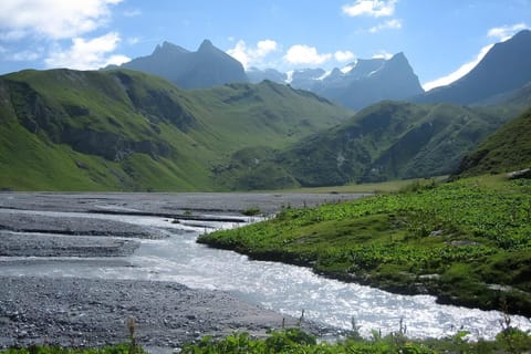 This picturesque scene captures the breathtaking beauty of the French Alps, showcasing a winding river cutting through a verdant valley with towering mountain peaks in the background. The landscape is a testament to the region's natural splendor and offer