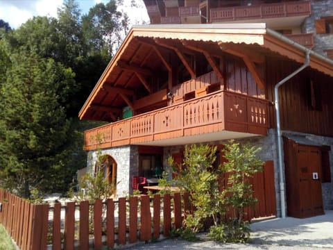 The chalet's exterior boasts a charming wooden facade with a traditional alpine design, featuring a balcony with intricate wooden railings.  The surrounding greenery adds a touch of natural beauty, while the stone accents lend a touch of rustic elegance. 