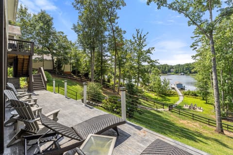 Spacious outdoor deck with lounge chairs overlooking a lush, tree-filled yard and serene lake views, offering a perfect spot for relaxation