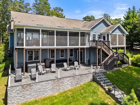 A stunning lakefront home with a spacious screened porch, surrounded by a lush green lawn and a charming stone pathway leading down to the water.