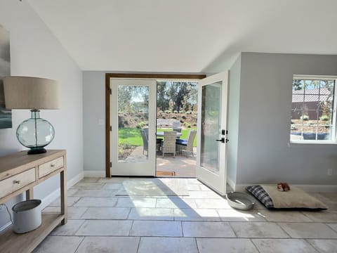 Large patio doors flood the room with natural light and lead to an inviting outdoor living space. Outside, you'll find multiple entertainment areas, including a cozy seating area, a dining set for alfresco meals, and a BBQ grill.