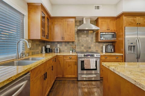 A sleek kitchen gleams with stainless steel appliances, including a side-by-side fridge and a 30” gas range with oven. Granite countertops and a large island offer ample prep space. Cabinets are filled with elegant dishware, cookware, and utensils.