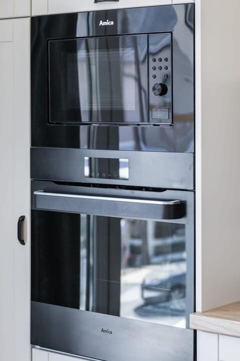 The image showcases a built-in oven and microwave, seamlessly integrated into tall white cabinetry reflecting the minimalist design, making the kitchen both functional and stylish.