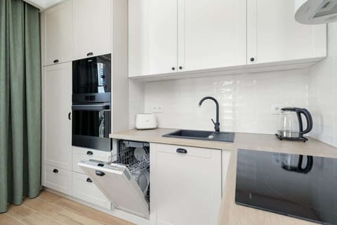 The kitchen features a clean, modern design with white cabinets, a marble-style countertop, and a black faucet paired with a matching black sink, creating a sleek contrast, while natural light from the nearby windows enhances the open and airy feel o