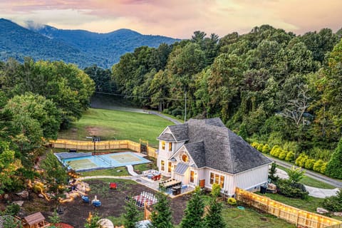 Enchanting modern home with magical outdoor living: fire pit with Adirondack seating, pickleball courts, and giant yard games. String lights and ambient lighting create the perfect evening.
