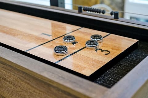 A stylish wooden shuffleboard table with black and silver pucks, perfect for indoor entertainment.