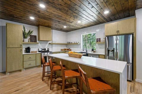Modern rustic kitchen with wood cabinetry, white quartz island, leather bar stools, stainless steel appliances, and natural light from large window.