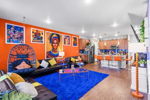 Relax in a colorful, art-filled living room that blends comfort with cultural flair, featuring striking wall art, bold orange accents, and luxurious leather couches for a truly unique experience