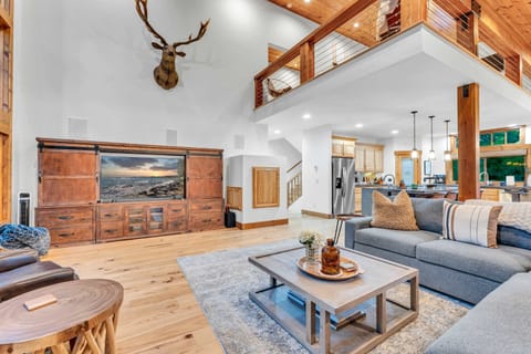 Living Room: Open layout to kitchen and dining room, L-shaped couch, wood-burning fireplace, 65” Smart TV, access to back and front decks