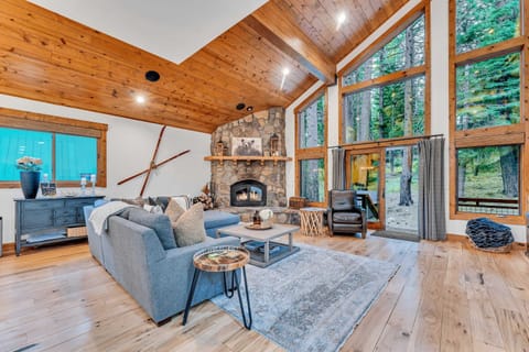 Living Room: Open layout to kitchen and dining room, L-shaped couch, wood-burning fireplace, 65” Smart TV, access to back and front decks
