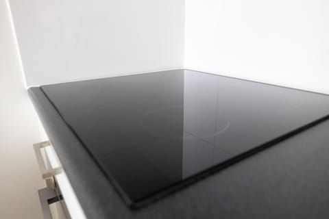 Sleek, modern induction cooktop with a glossy black surface, seamlessly integrated into a black countertop. The minimalist design offers a smooth finish and easy cleaning, ideal for efficient and contemporary cooking spaces. Perfect for creating a stylish and functional kitchen experience.