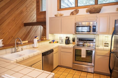A modern kitchen with beige cabinetry, stainless steel appliances, a tiled countertop, and a diagonal wood accent wall. Various utensils and decor items are neatly arranged on the counters.