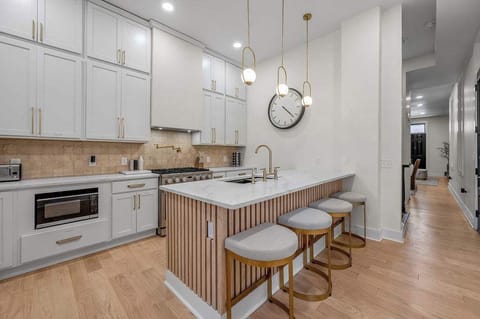 Contemporary kitchen featuring crisp white cabinets, stainless steel appliances, and a spacious island with bar seating. Ideal for cooking and entertaining, with elegant lighting and a charming bar cart by the window.