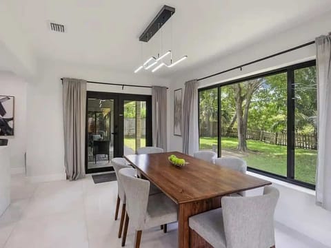 Gather around the dining area, beautifully illuminated by floor-to-ceiling glass windows that offer stunning views of the lush backyard, blending indoor comfort with outdoor serenity.