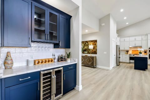 Modern wet bar with navy cabinets, a wine fridge, and a sleek countertop, seamlessly connected to a bright open kitchen and living area.