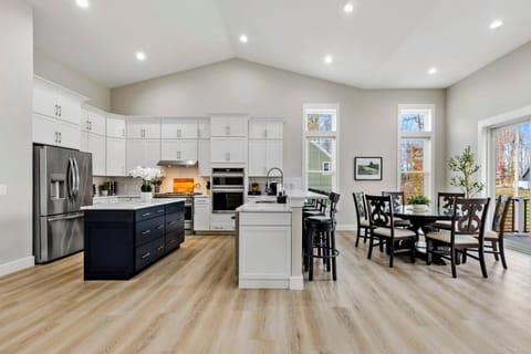 Bright open-concept kitchen and dining area with white cabinets, a navy island, and large windows providing natural light and scenic views.