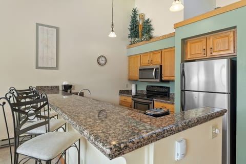 Full kitchen featuring stainless steel appliances, granite countertops, and breakfast bar seating three.