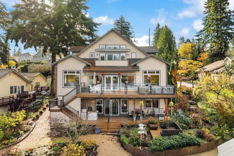 This stunning three-story lakeshore home features a modern design with large windows, natural stone accents, and warm wood details. The inviting front porch and beautifully landscaped gardens set the stage for a serene lakeside retreat, with balcony.