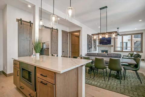 - Open kitchen and dining space with island seating and modern pendant lighting
- View extends to a cozy living area with fireplace for seamless entertaining
- Barn doors and warm wood tones add rustic charm to the open layout