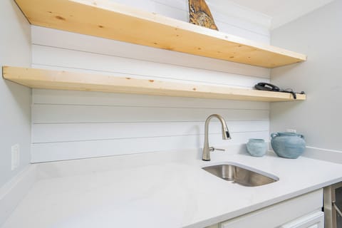 This wet bar features sleek white cabinetry, a stainless sink, and decorative blue vases, perfect for entertaining